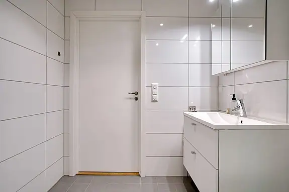 Badet er utstyrt med dusjhørne med innfellbare dører, veggmontert wc, baderomsinnredning og opplegg for vaskemaskin