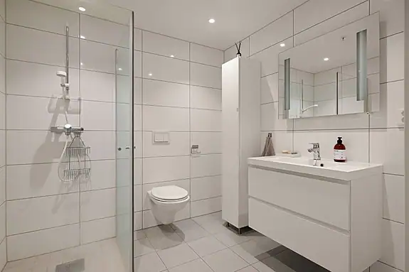 Badet er utstyrt med dusjhjørne, veggmontert wc, baderomsinnredning og speil med integrert belysning