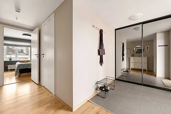 Romslig entre med flislagt gulv, praktisk skyvedørsgarderobe og plass til skohylle