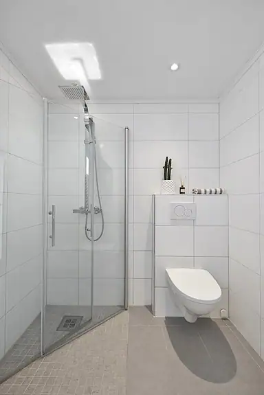 Badet er utstyrt med baderomsinnredning, veggmontert wc og dusjhjørne med innfellbare dører