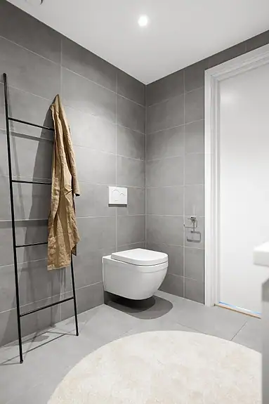 Badene i boligen har samme materialvalg og er innredet med veggmontert wc, baderomsinnredning, dusjhjørne og speil med integrert belysning