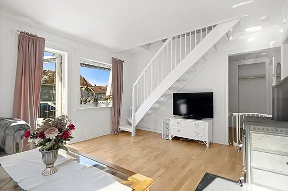 Lyse overflater, parkett og vinduer på to sider gir stuen en luftig og innbydende atmosfære, med plass til både sofagruppe og TV-møbler.
